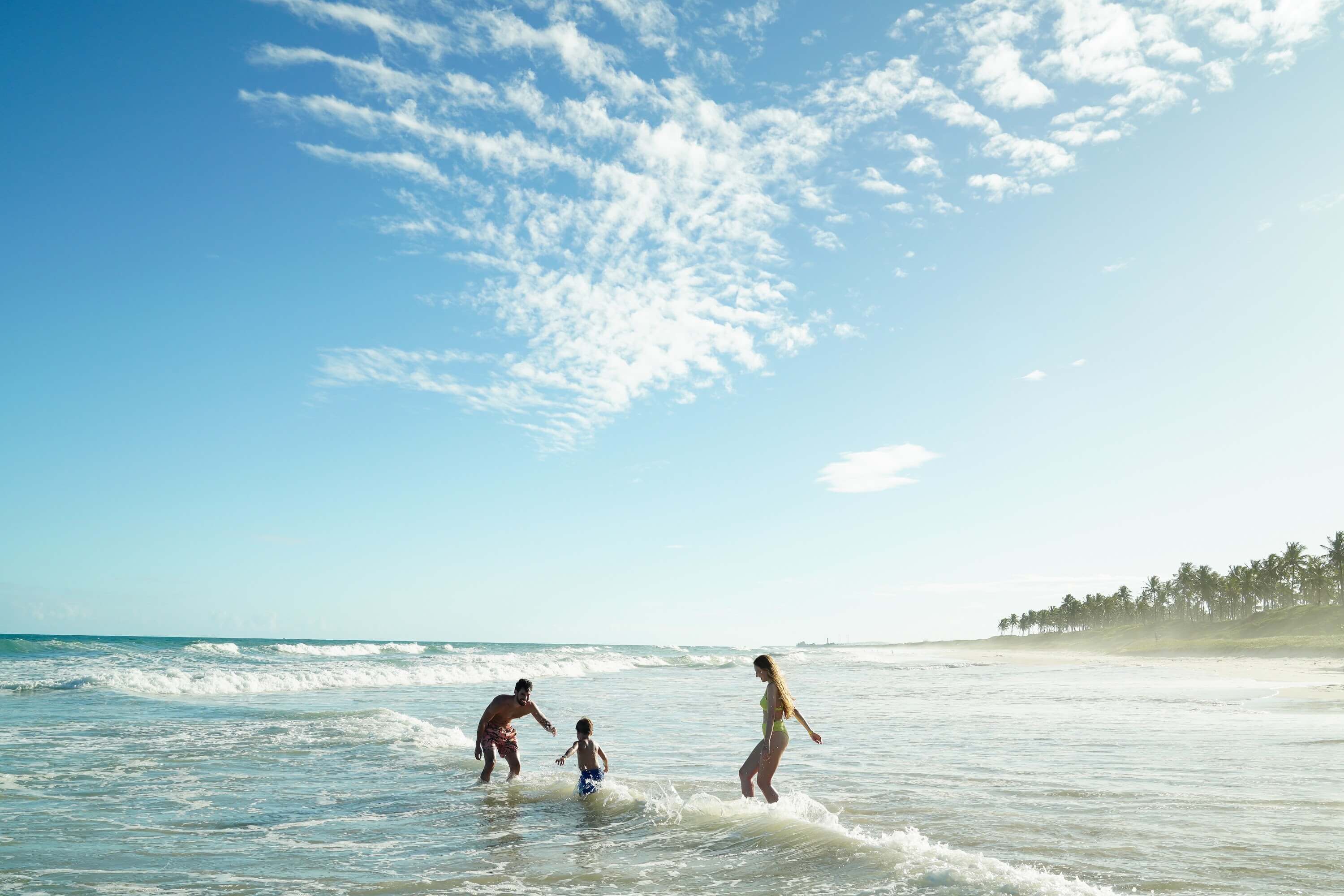 Família feliz brincando dentro do mar na praia do Francês, em Alagoas.